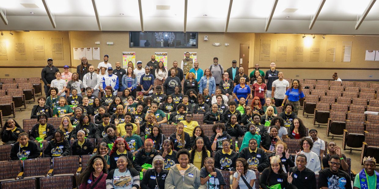 A large group of diverse people posing in a spacious auditorium with many empty seats.
