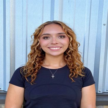 Smiling woman with curly hair wears a black shirt and cross necklace.