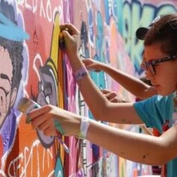 People creating colorful graffiti art on a wall with spray paint.