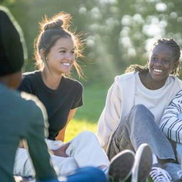 Group of friends sitting outdoors enjoying a sunny day and smiling.