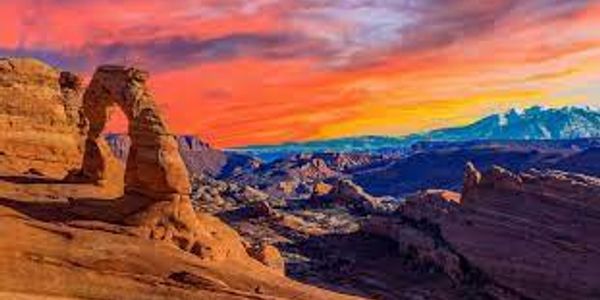 Sunset over a natural rock arch in a desert landscape.