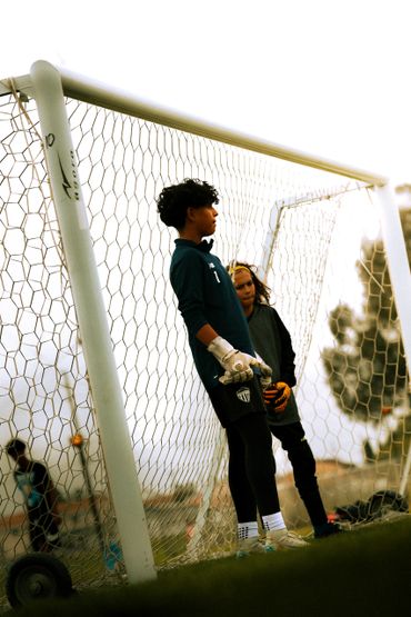 Two young soccer goalkeepers standing near the goalpost on a field.