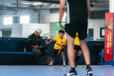 Kids playing indoor soccer with a coach or parent watching.