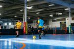 Two players in an indoor futsal match actively chasing the ball.