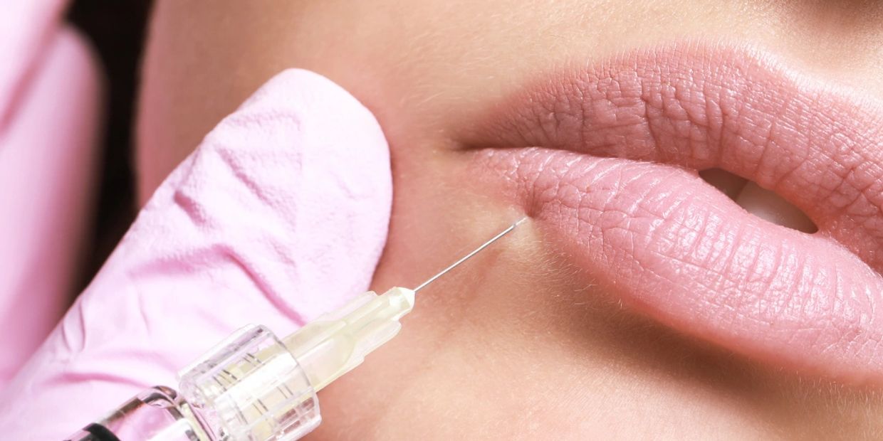 A close-up photo of a syringe and needle against a woman's lips. 