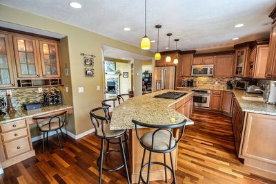 Hardwood flooring in farm-inspired light wood colored kitchen with granite countertops on all surfaces.