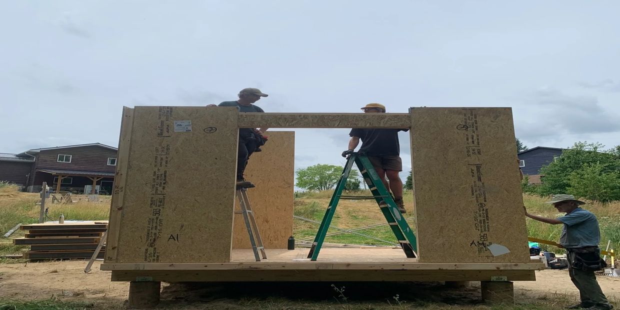 Three people assembling a wooden structure on ladders outdoors.