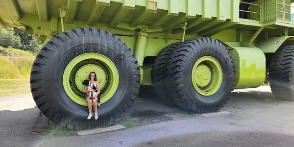 Woman sitting inside the giant tire of a large green mining truck.