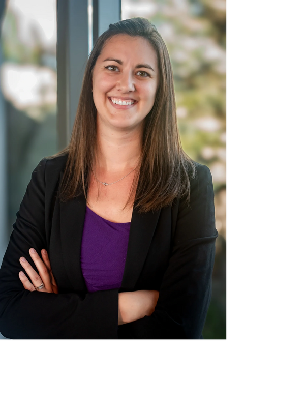 Confident woman smiling with arms crossed, wearing a black blazer and purple top.