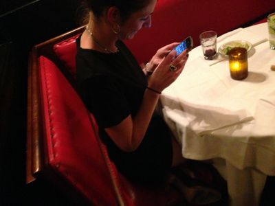 Woman sitting in a red booth looking at her phone at a restaurant.