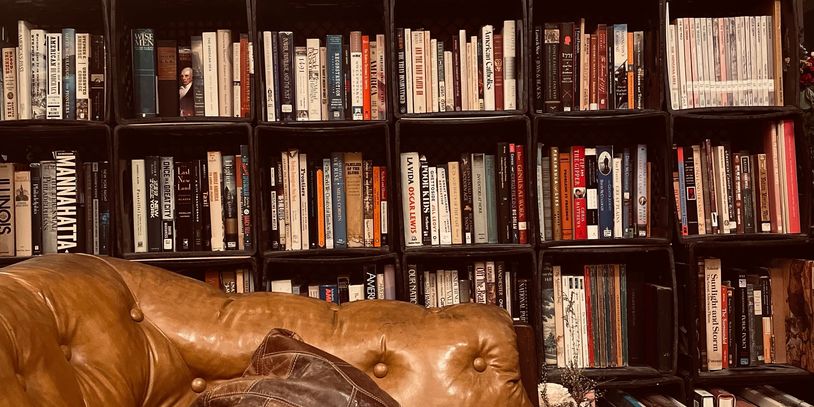 Cozy leather couch in front of a large bookshelf filled with books.