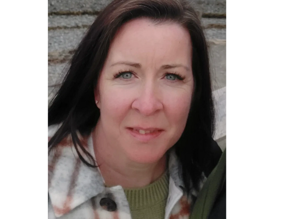 Woman with dark hair and blue eyes wearing a plaid coat and green sweater.