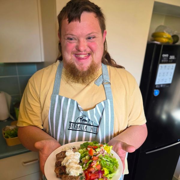 Smiling chef presenting a plate of fresh salad and meat.