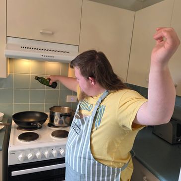 Person in apron pouring oil in the kitchen.
