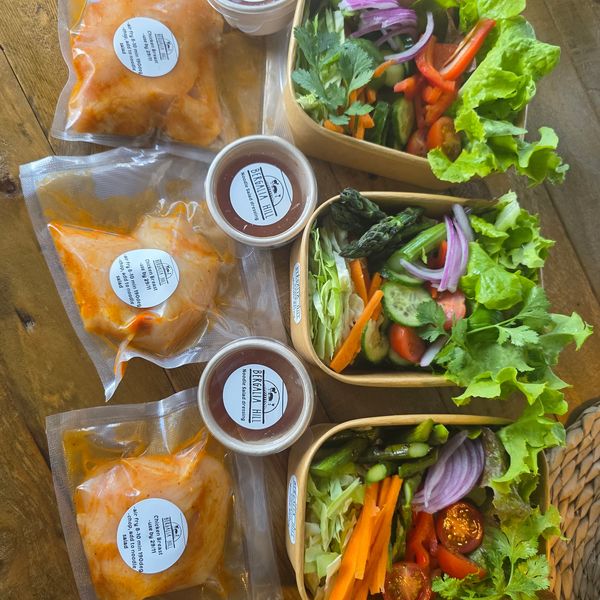 Three fresh salad bowls with packaged sauces and marinaded chicken.