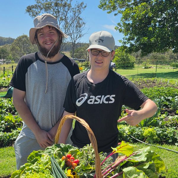 Two young men with a basket of fresh vegetables in a garden.