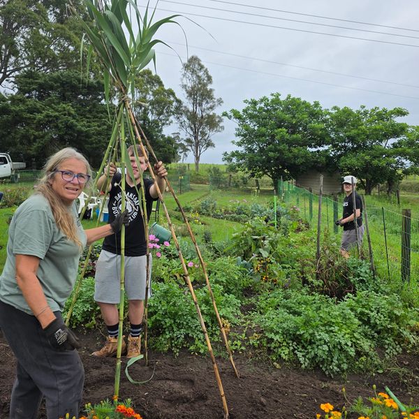 Three people building a garden structure outdoors.