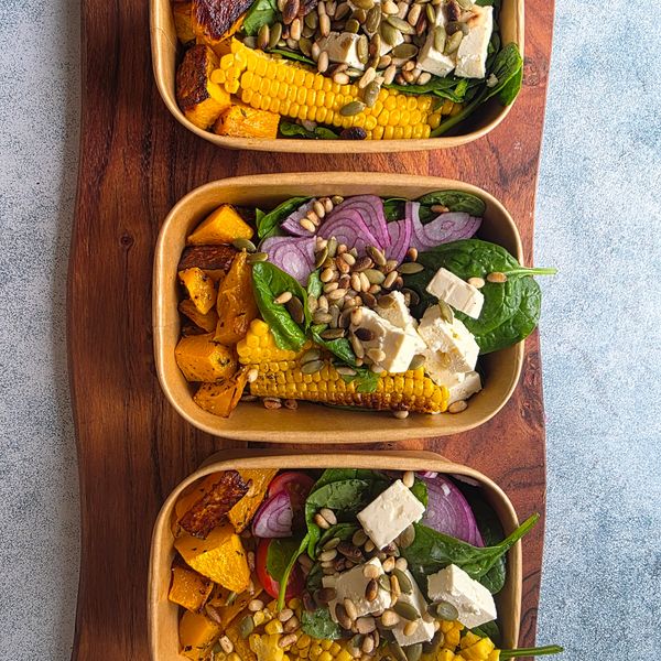 Three bowls of healthy salad with corn, tofu, spinach, and seeds.