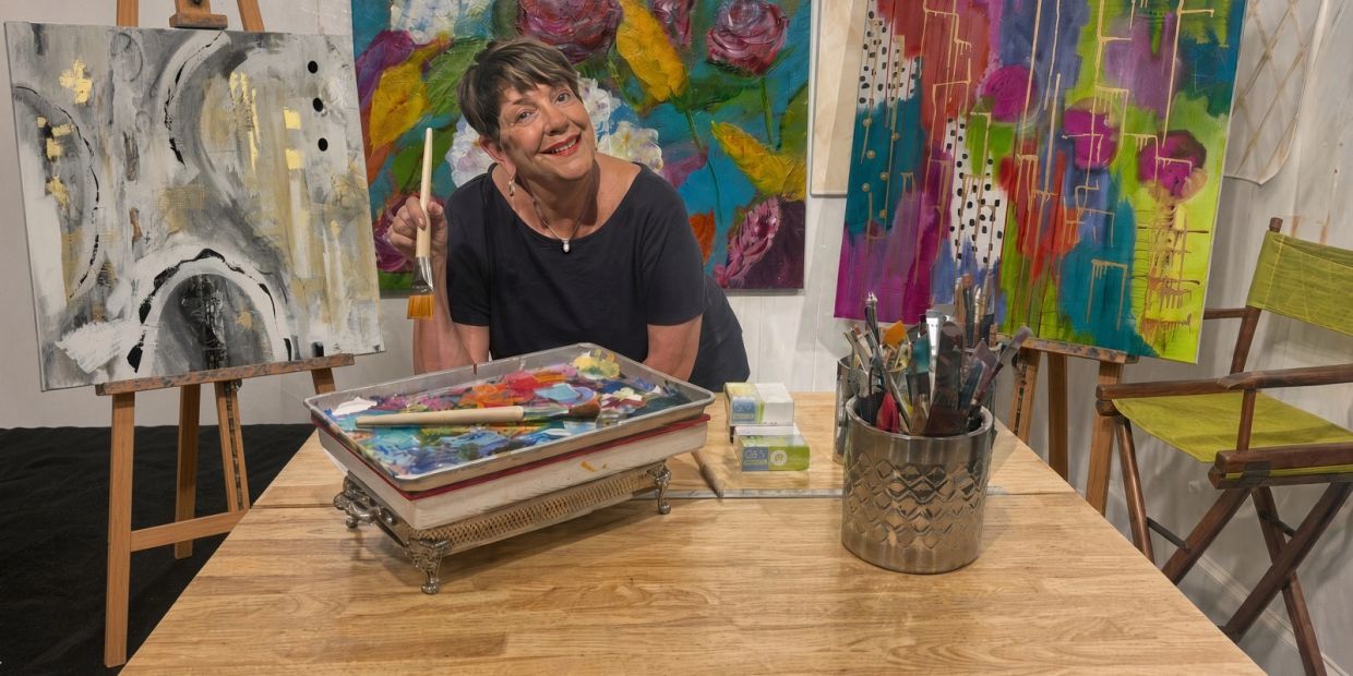 A woman artist smiling with her painting tools and canvases.