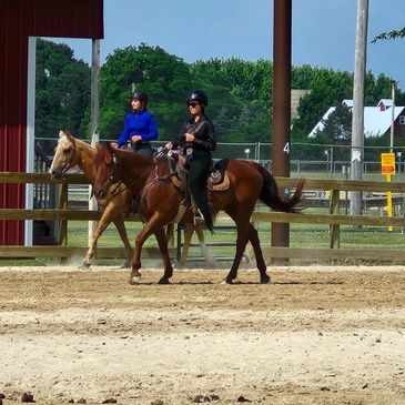 Two people horseback riding in an outdoor arena.