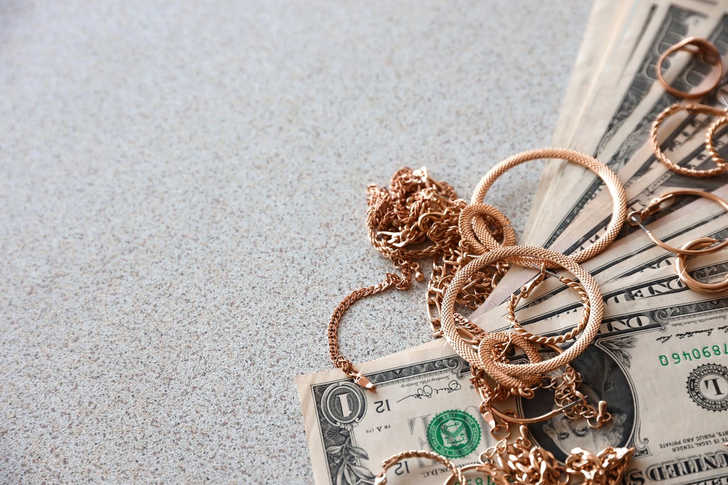 Gold jewelry placed on top of US one-dollar bills on a textured surface.