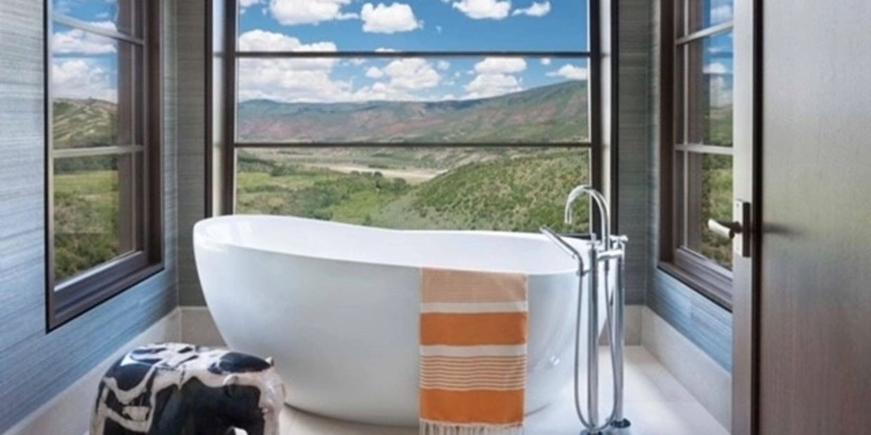 Modern bathroom with a freestanding tub overlooking scenic hills and blue skies.