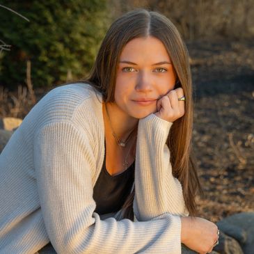 Young woman with long brown hair resting her chin on her hand outdoors.