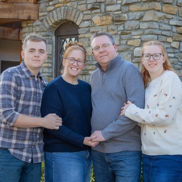 A family of four standing together outside a stone house, smiling.