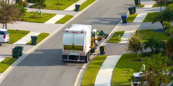 Garbage truck collecting trash bins on a residential street.