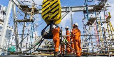 Workers in orange uniforms using crane on construction site.