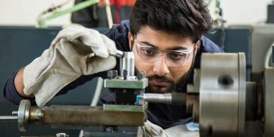 Man operating precision measuring instrument on lathe.