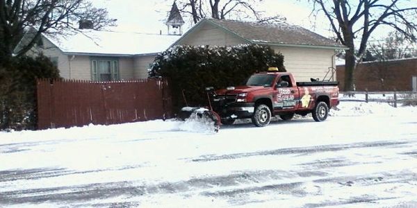 A maroon Big Earl's Stump Removal truck with a plow sitting in a plowed parking lot.