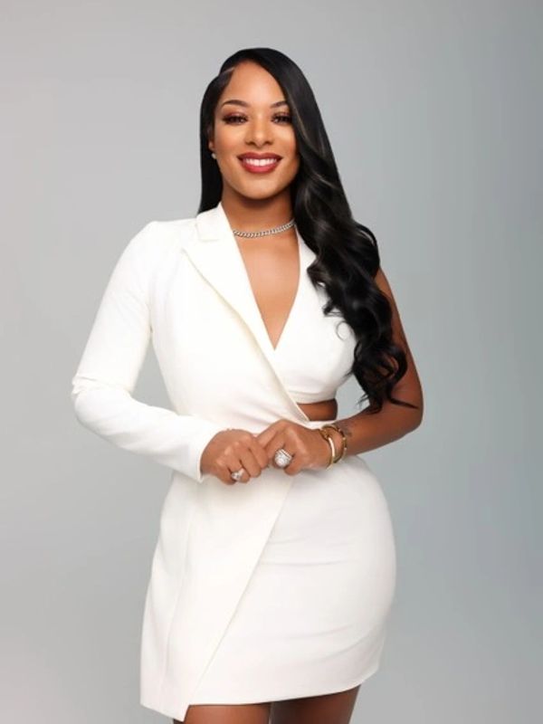 Confident woman in a stylish white asymmetrical dress smiles at the camera.