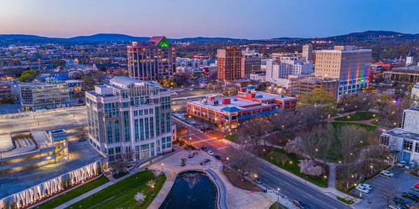 A vibrant cityscape at dusk with modern buildings and a small pond.