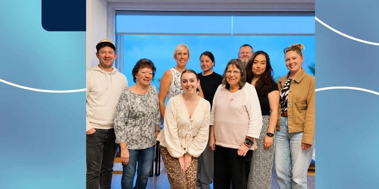 A group of nine people posing indoors with a blue window background.