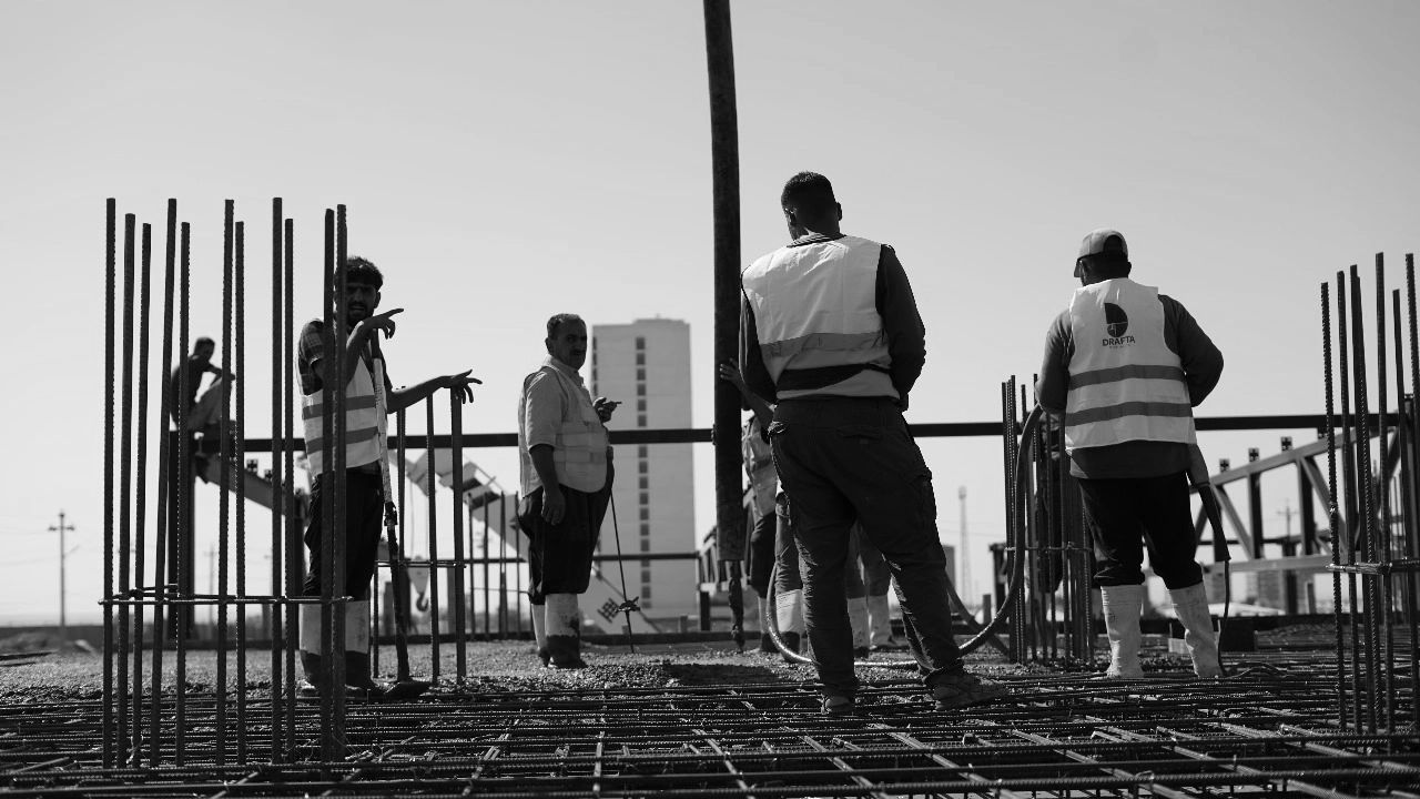 Workers in safety vests working on a concrete construction site under clear skies.