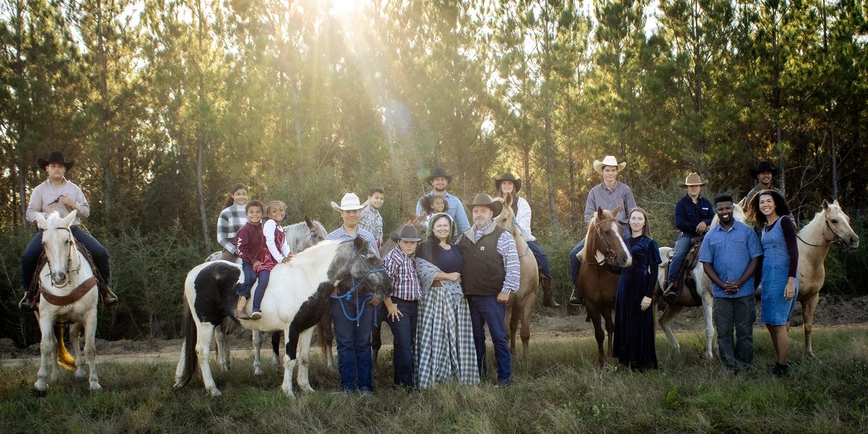 A large family poses outdoors with horses in the golden sunlight.