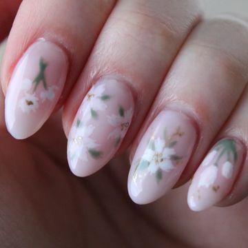 Soft pink nails with delicate white floral designs and green leaves.