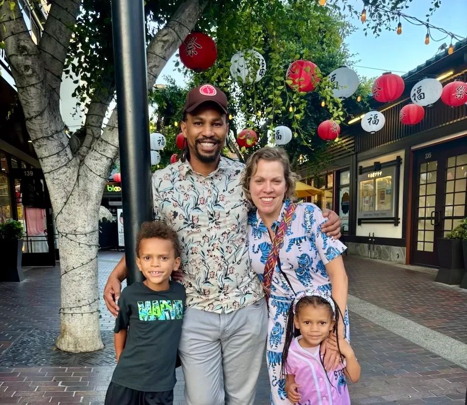 Happy family of four posing outdoors with festive lanterns overhead.