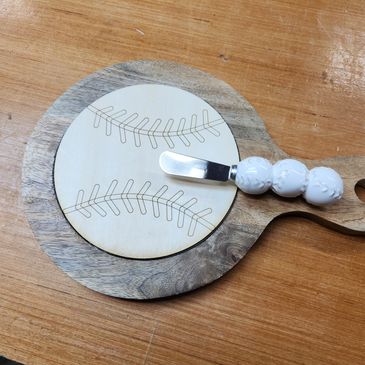 Wooden cheese board with baseball design and white-handled spreader.