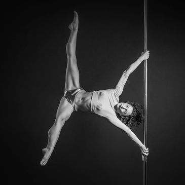 Pole dance instructor demonstrates advanced pole fitness move Iron X. A variation of human flag.