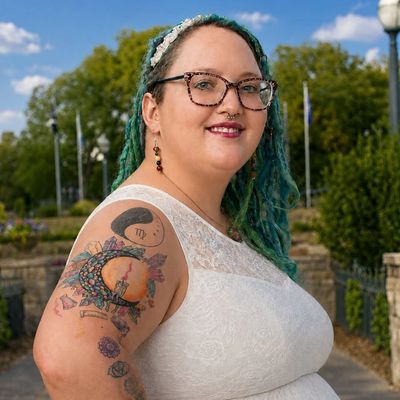 Smiling woman with glasses and colorful tattoos outside.