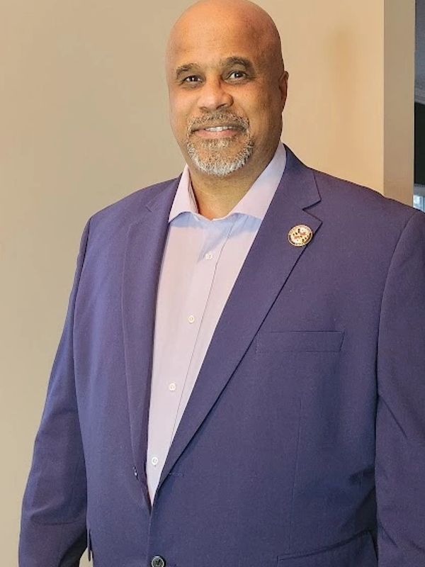 A smiling man in a purple blazer and light shirt.