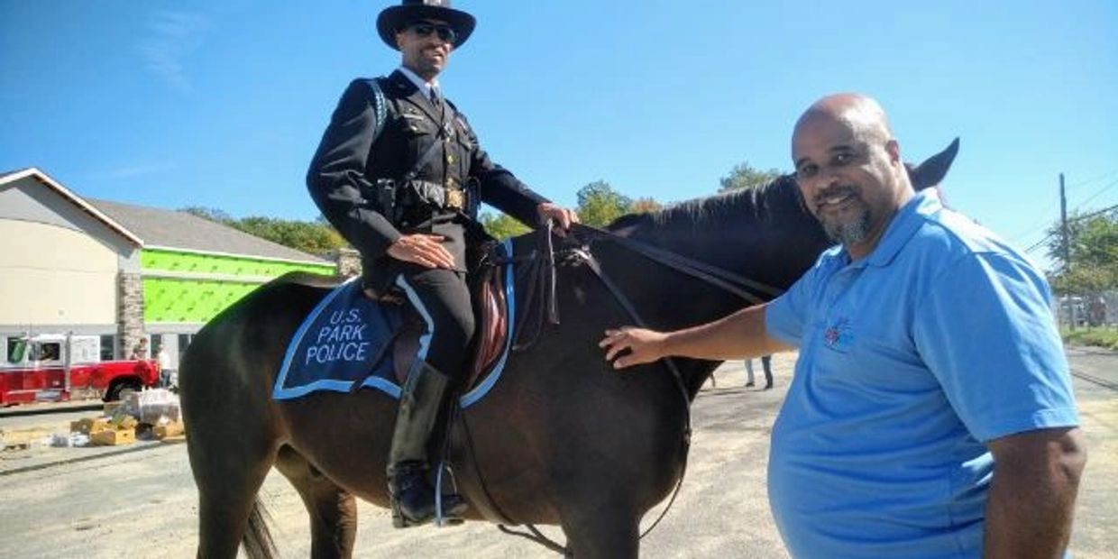 A mounted U.S. Park Police officer and a man petting the horse on a sunny day.