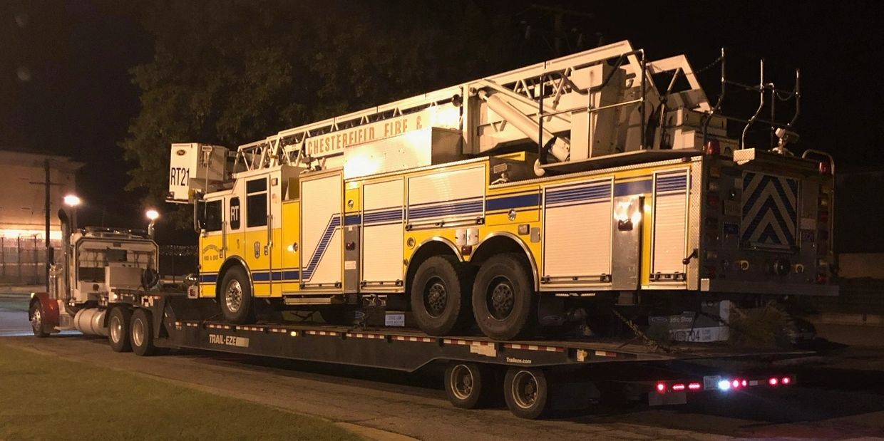 Large truck towing a large fire truck on a trailer