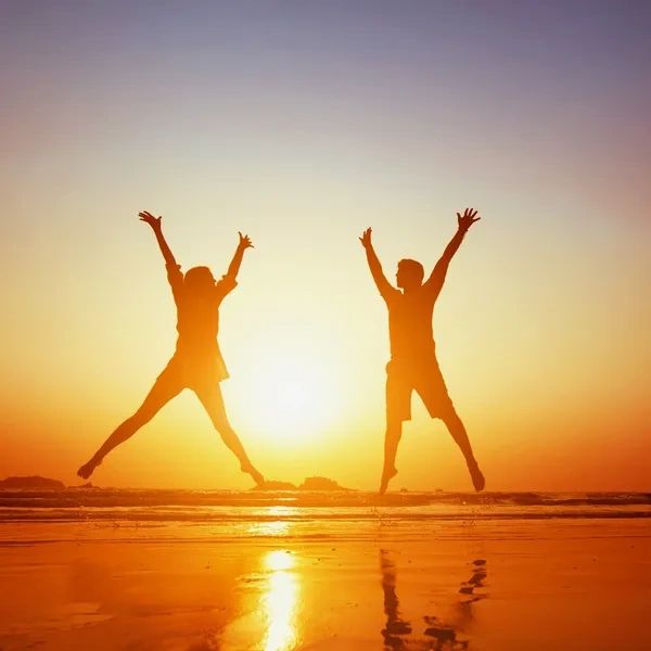 Two people jumping joyfully on the beach at sunset.
