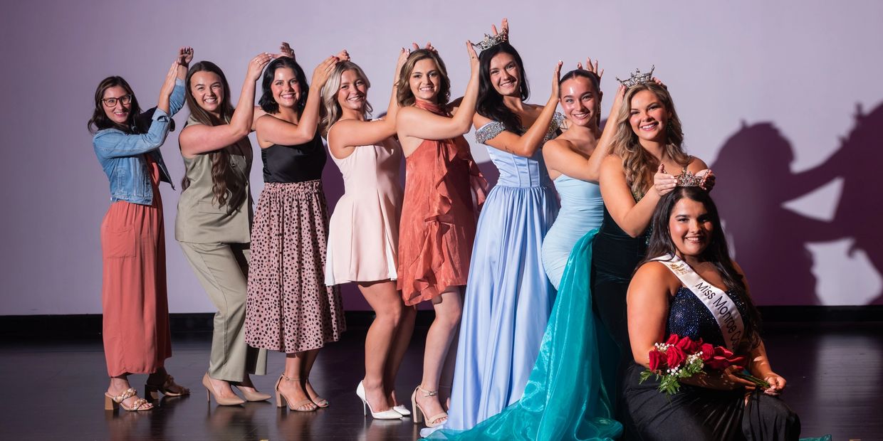 A group of women crowning a beauty queen holding roses and wearing a sash.