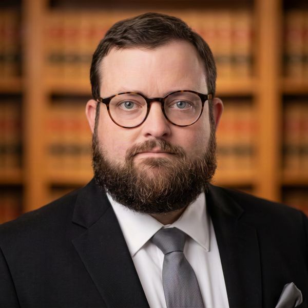 Bearded man in glasses and suit with lawyer background.