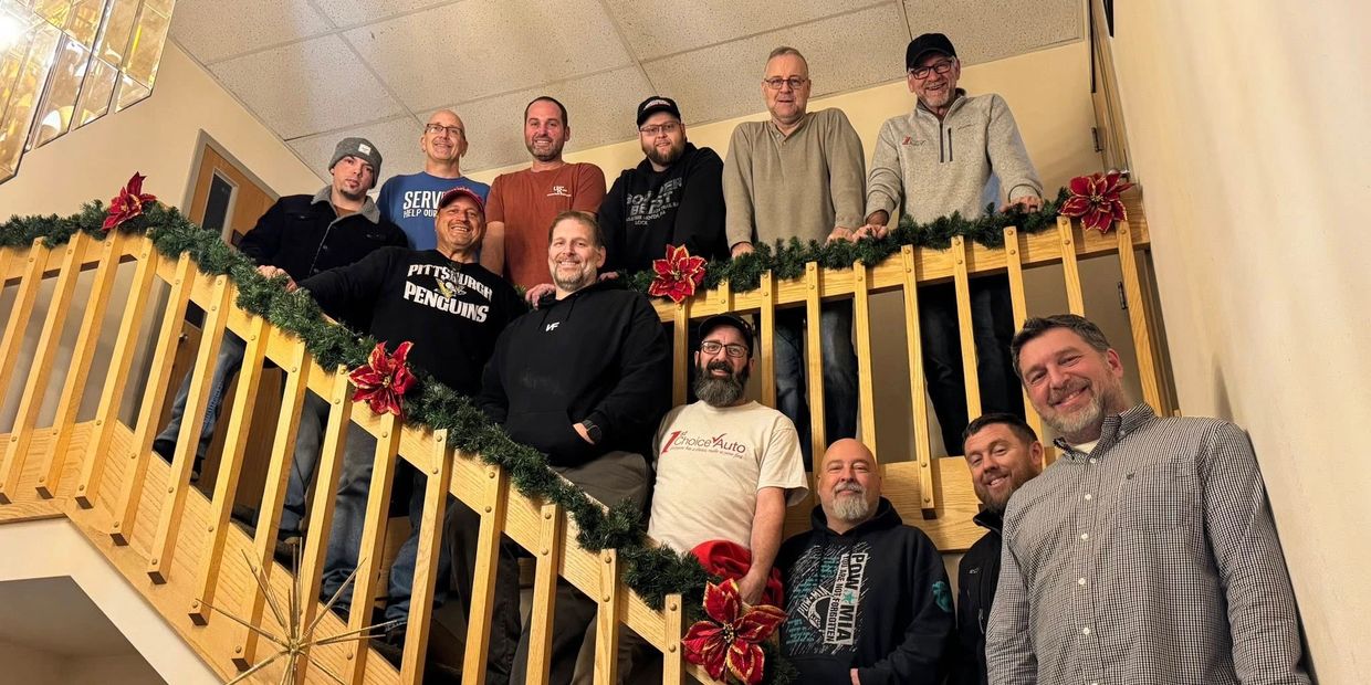 Group of men smiling on a decorated staircase for a holiday gathering.