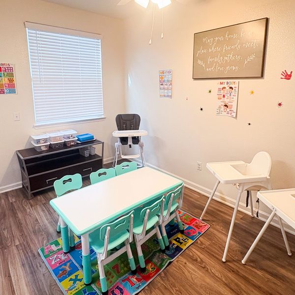 Bright children's playroom with small tables, chairs, and educational posters.